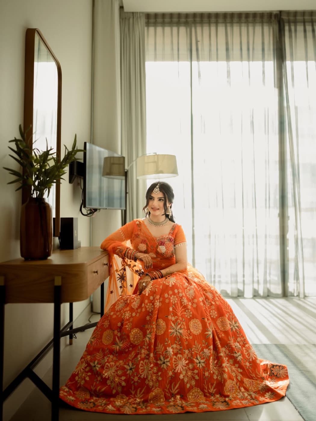 Bride in orange bridal wear by a window